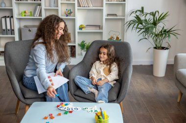 Konuşma terapistlerinin ofisinde. Uzun saçlı kadın konuşma terapisti bir kızla seans yapıyor.