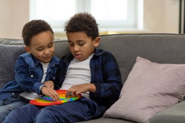 Neşeli çocuklar ellerinde rengarenk baloncuklar tutarak popüler silikon oyuncakların üzerine baloncukları itiyor duyusal oyunun tadını çıkarıyorlar koltukta dinlenmek için.