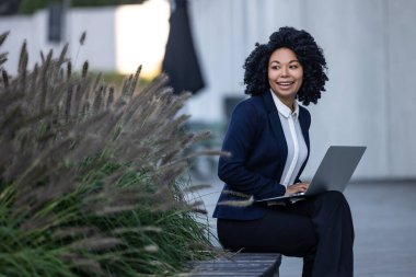Açık havada çalışmak. İş merkezinin yanında otururken dizüstü bilgisayarda çalışan güzel bir iş kadını.