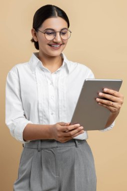 Profesyonel kullanım için dijital tablet tutan neşeli iş kadını bej arka planda tek başına duruyor