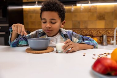 Kahvaltı vakti geldi. Esmer tenli çocuk masada oturuyor ve kahvaltı yapıyor.