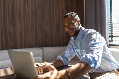 Genç esmer adam ofisinde masasında oturuyor ve dizüstü bilgisayarla çalışıyor.