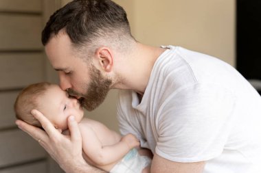 Beyaz sakallı, genç bir baba yeni doğmuş bir bebeği öpüyor.