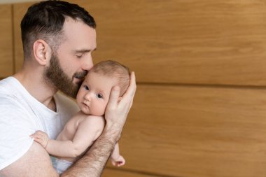 Beyaz sakallı, genç bir baba yeni doğmuş bir bebeği öpüyor.