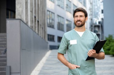 Laboratuvar önlüğündeki sakallı doktor elinde hastane notlarıyla dolu bir dosya tutuyor.