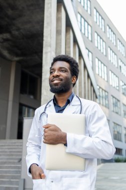 Dışarıda duran yakışıklı genç doktor bir elinde dizüstü bilgisayarla hastalarla çevrimiçi bağlantı kurmaya hazır.