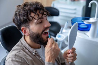 Diş telleri olan bir adam diş fırçasıyla dişlerini titizlikle fırçalayıp diş telleri ve ayraçlar arasına ulaşarak ağız sağlığını koruyor.