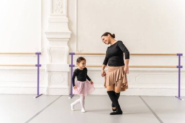 Zarif bayan öğretmen dans dersinde stüdyoda küçük kız balerine egzersizi anlatıyor.