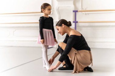 Klasik bale dersinde genç bir kızı çalıştıran zarif hareketlerine yardımcı olan zarif bir bayan antrenör.