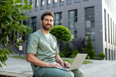 Kafkasyalı sağlık çalışanı dizüstü bilgisayarla hastane yakınlarında internette yazı yazıyor.