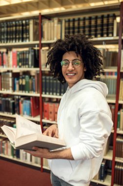 Kitap kurdu. Kütüphanede gözlüklü kıvırcık saçlı genç adam.