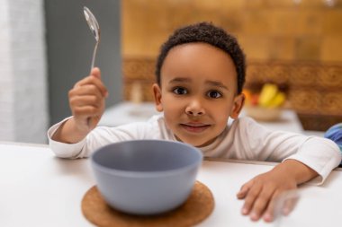 Kahvaltıda. Koyu tenli çocuk masada oturup mısır gevreği yiyor.