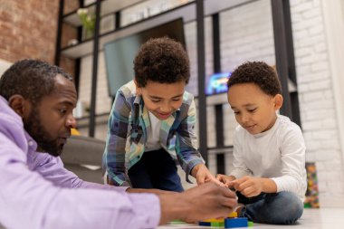 Jenga oynuyorum. Koyu tenli bir adam çocuklarıyla Jenga oynuyor ve olaya dahil olmak istiyor.