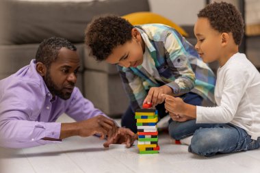 Jenga oynuyorum. Koyu tenli bir adam çocuklarıyla Jenga oynuyor ve olaya dahil olmak istiyor.