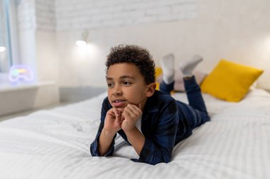 Rüya gibi. Kıvırcık saçlı, koyu tenli çocuk yatakta uzanıyor ve düşünceli görünüyor.