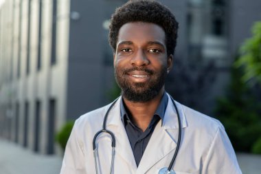 Gülümseyen Afrikalı Amerikalı doktor hastane dışında üniformalı, yorucu bir günün ardından dinleniyor.