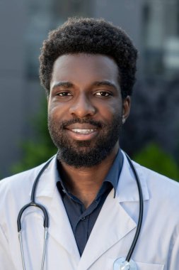 Gülümseyen Afrikalı Amerikalı doktor hastane dışında üniformalı, yorucu bir günün ardından dinleniyor.