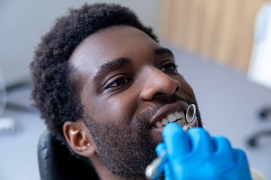 Modern ofisteki profesyonel dişçi Afrikalı Amerikalı hastaların diş etlerini diş aletleriyle kontrol ediyor.