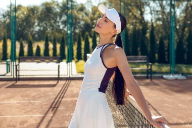 Gülümseyen tenisçi. Tenis kortlarında mutlu ve gülümseyen güzel bir genç kadın.