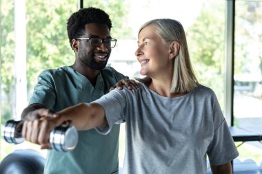 Rehabilitasyon egzersizleri. Kadın bir hastayla rehabilitasyon egzersizleri yapan Afrikalı Amerikalı bir doktor.