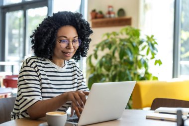 Kahve ve iş. Çizgili bluzlu kadın dizüstü bilgisayarda çalışıyor ve kahve içiyor.
