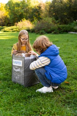 Küçük çocuklar parktaki çöpleri topluyorlar toplum projesine katılıyorlar ekolojiyi destekliyorlar
