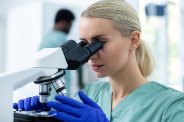 Steril laboratuardaki biyokimyasal örnekler üzerinde yoğunlaşmak için modern mikroskop ve ekipman kullanan klinikteki kadın doktor.