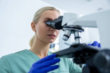 Laboratuvardaki profesyonel kadın teknisyen, bilimsel yenilik araştırmalarında test için mikroskop altında numunelere bakıyor.