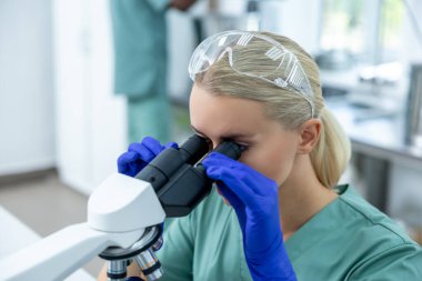 Steril laboratuardaki biyokimyasal örnekler üzerinde yoğunlaşmak için modern mikroskop ve ekipman kullanan klinikteki kadın doktor.