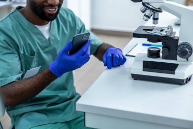 Laboratuvarda deney yapan Afrikalı Amerikalı bilim adamı cep telefonu ve mikroskop kullanarak örnekler üzerinde testler yapıyor.