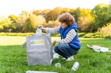 Beyaz erkek çocuk, çevre faaliyetleri ve geri dönüşümle ilgilenmek için toplum etkinliği sırasında plastik atık topluyor.