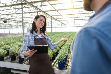 Sohbet. Önlüklü, gülümseyen genç bir kadın bir erkekle konuşuyor ve olumlu bakıyor.