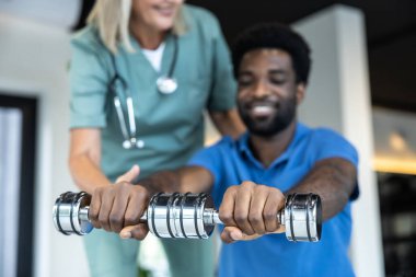 Fizik tedavi. Kolları üzerinde çalışan Afrikalı Amerikalı genç bir adam, ona rehberlik eden kadın bir doktor.