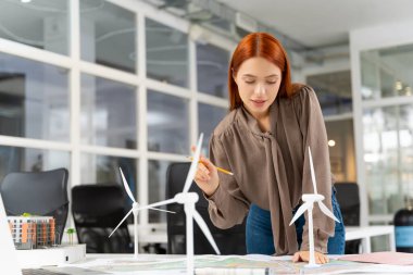 Ofiste çalış. Ofiste çalışan kızıl saçlı kadın. Odaklanmış ve ilgili görünüyor.