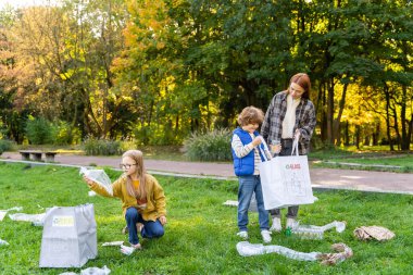 Çocuklar çevre bakımı için plastik atıkları geri dönüşüm poşetlerine ayıran öğretmenleriyle birlikte çöpleri topluyorlar.