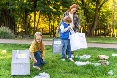 Çocuklar çevre bakımı için plastik atıkları geri dönüşüm poşetlerine ayıran öğretmenleriyle birlikte çöpleri topluyorlar.