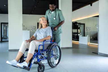 Doktor, tekerlekli sandalyedeki yaşlı kadına yardım ediyor ve cesaret verici bir konuşma yapıyor. Fizyoterapist ve yaralı bir kadın hasta iletişim kuruyor.