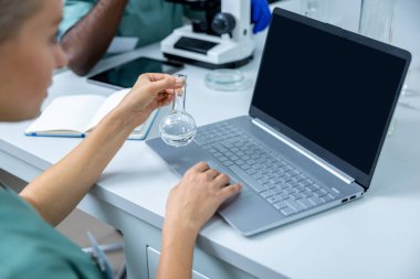 Bilim adamı olarak çalışan ceketli bir kadın biyoteknolojide online araştırma ve veri analizi için dizüstü bilgisayar kullanıyor.