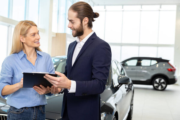 Подписываю контракт. Блондинка-клиент подписывает контракт с представителем дилерского центра