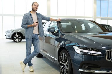 Araba galerisindeki adam. Bir araba galerisinde yeni bir arabanın yanında duran kendine güvenen beyaz bir genç.