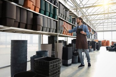 Sakallı erkek, mağazadaki raflarda küçük işletme muhasebe saksılarının sahibi.