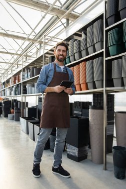 Dükkandaki sakallı adam, küçük işletmeleri yönetirken dükkandaki raflardaki bitkiler için plastik kaplarla çevrili.