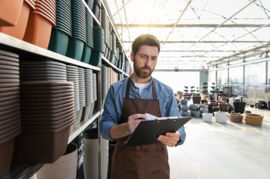 Çekici erkek bahçe merkezi çalışanı ot reyonunda notlar alıyor.