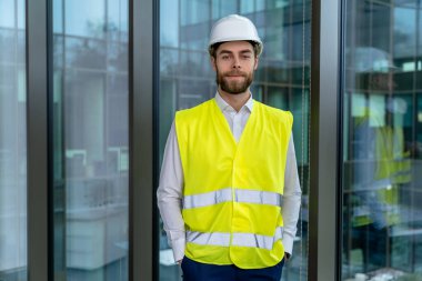 Erkek mühendis. Sarı yelekli ve koruyucu şapkalı genç erkek mühendis kararlı görünüyor.