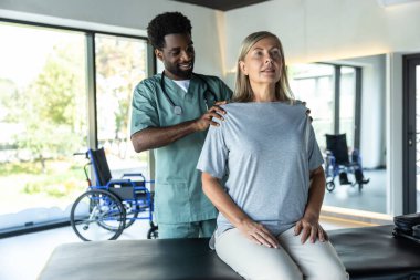 Duruş düzeltmesi. Afrika kökenli Amerikalı erkek doktor kadın hastaların duruşlarını düzeltmeye çalışıyor.