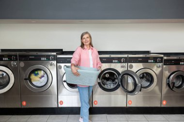 Çamaşırhanedeki kadın. Elinde sepetle çamaşırhanenin yanında duran olgun, beyaz bir kadın.