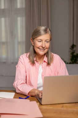 Çalışan bayan. Gülümseyen orta yaşlı bir kadın dizüstü bilgisayarda çalışıyor ve ilgili görünüyor.