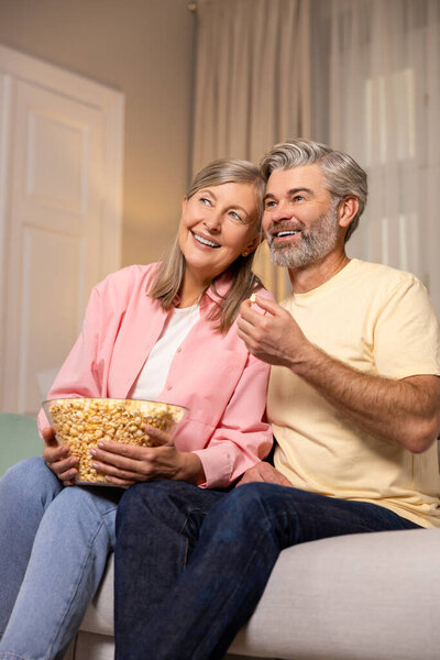Peaceful evening at home. Mature couple spending time together at home and eating popcorn.