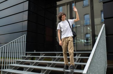 Öğrenci. Beyaz tişörtlü uzun boylu beyaz adam binanın girişindeki merdivenlerde.