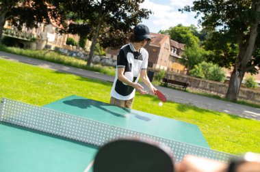 Masa tenisi oynuyorum. Siyah şapkalı adam masa tenisi oynuyor ve odaklanmış ve aktif görünüyor.